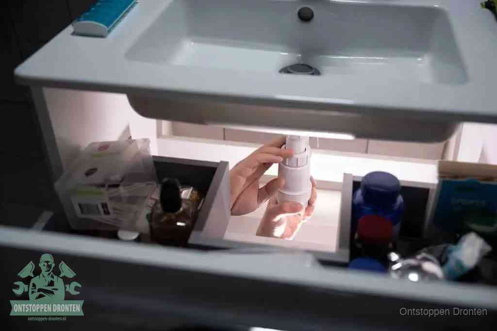 Een pompfles met zeep boven een wastafel, de heet water en afwasmiddel-methode om een vetprop in de afvoer los te maken in Dronten