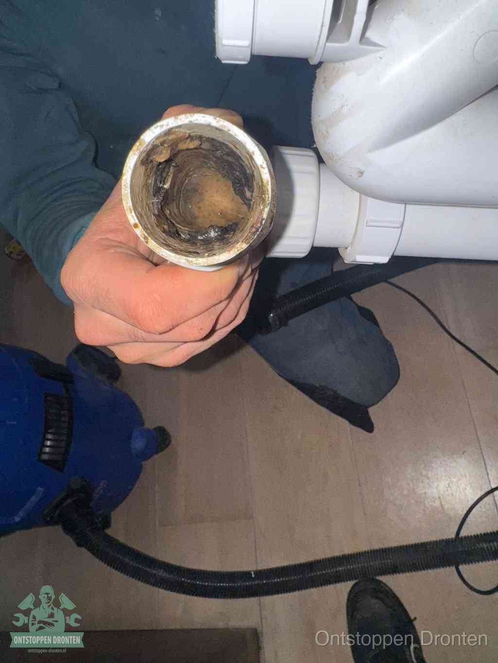 Een hand houdt een losgekoppeld PVC-afvoerbuisstuk vast dat van binnen volledig is dichtgeslibd met vet, vuil en aanslag, de meest voorkomende oorzaak van een verstopte afvoer in Dronten