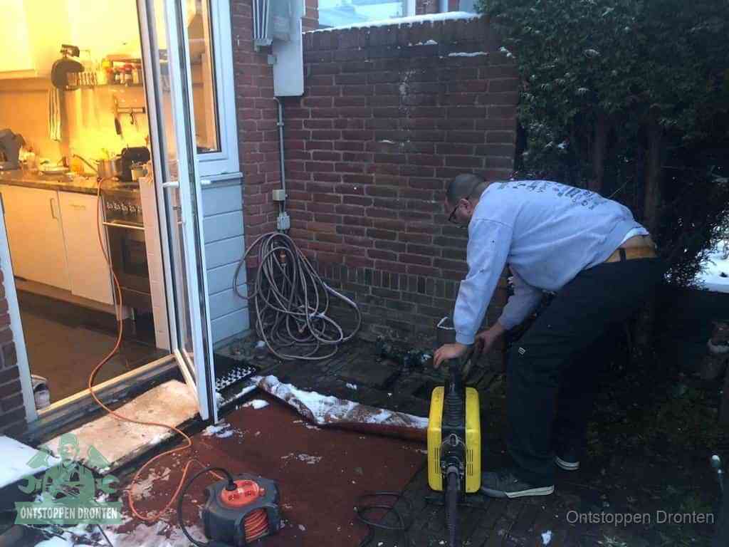 Een monteur werkt buiten bij een open riool-/grondput met een elektrische ontstoppingsmachine om een verborgen afvoerprobleem op te sporen in Dronten