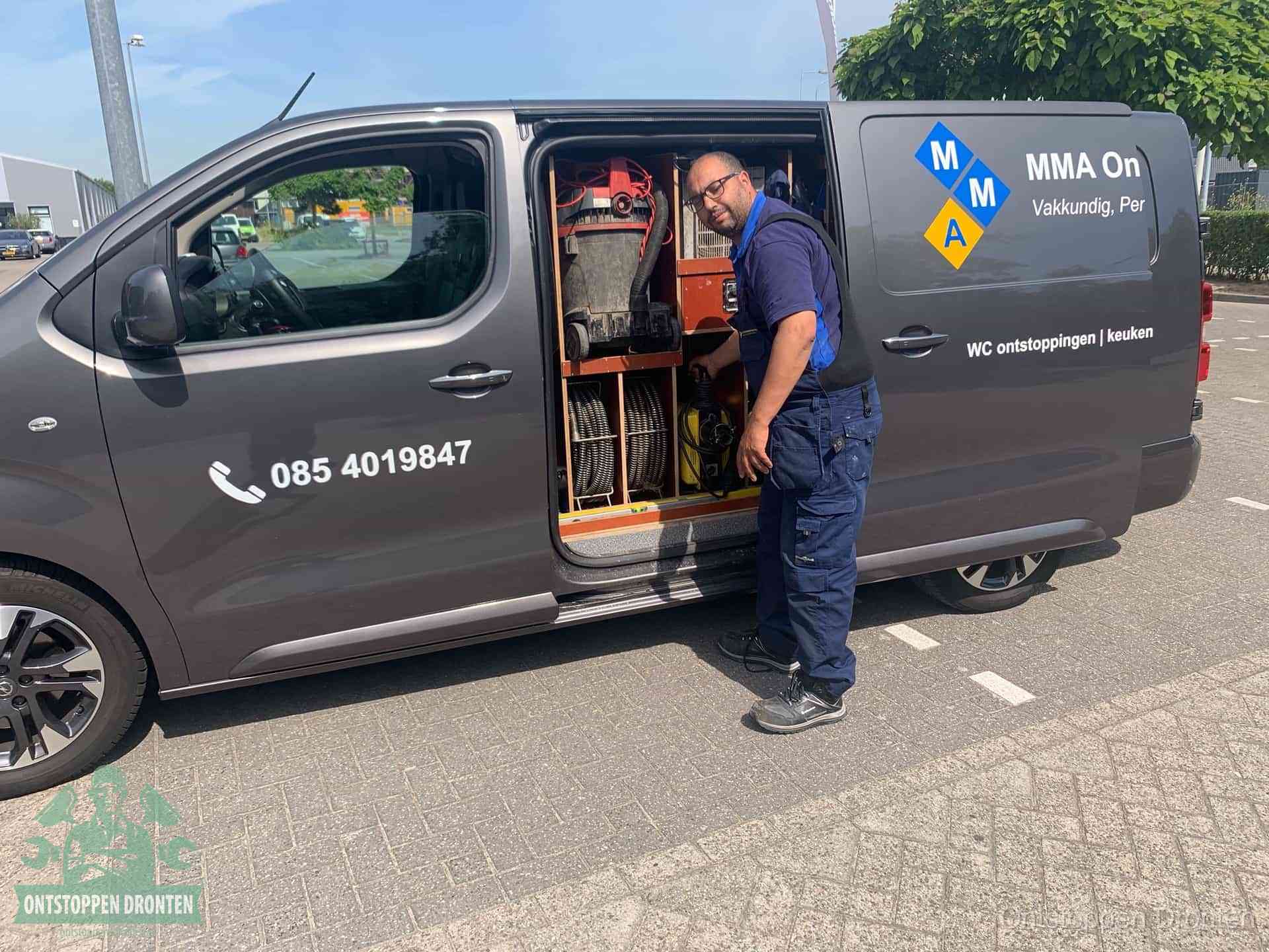 Een monteur bij de open schuifdeur van zijn bedrijfsbus op een parkeerplaats, klaar om de oorzaak van terugkerende afvoerverstoppingen aan te pakken in Dronten
