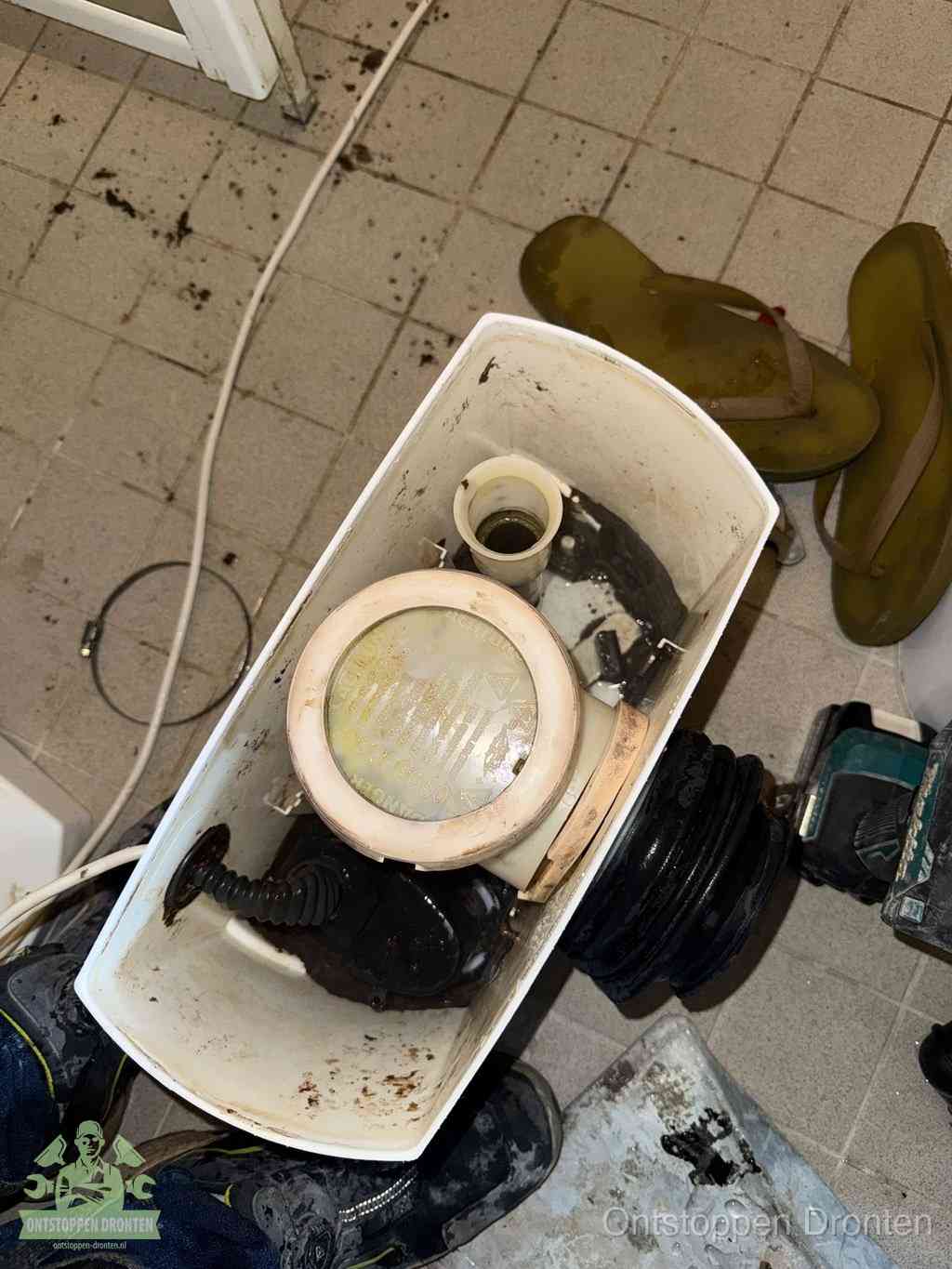Een gedemonteerde toiletpot op de vloer met ontstoppingsveer en gereedschap ernaast, het verwijderen van een vastzittend voorwerp uit de wc in Dronten