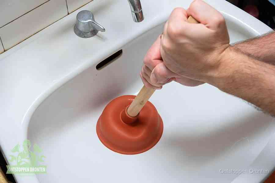 Twee handen gebruiken een rode rubberen plopper op een sanitair-afvoer om het toilet te ontstoppen in Dronten
