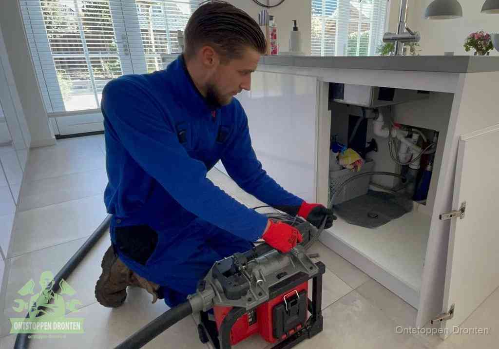 Een monteur voert een professionele elektrische ontstoppingsmachine in de afvoer onder de spoelbak tijdens het gootsteen ontstoppen in Dronten